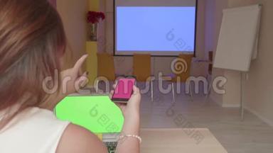 大厅里坐在桌旁的女孩的后视图，通过智能手机一键将图片发送到投影仪